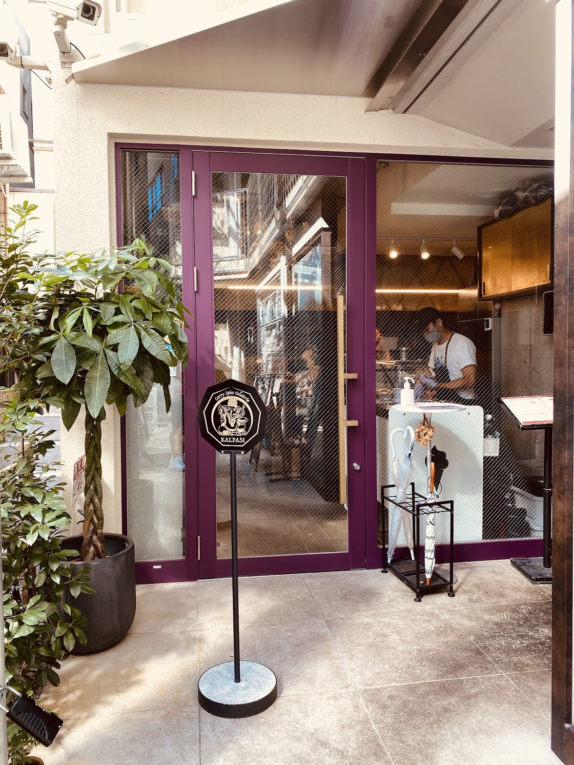 紫色のガラスドアの前にKALPASIのサインボードが立ち、店内でスタッフが作業している外観